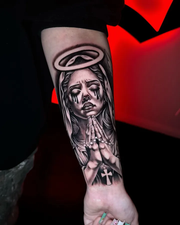 Black and grey tattoo by Dre: praying woman with halo, forearm