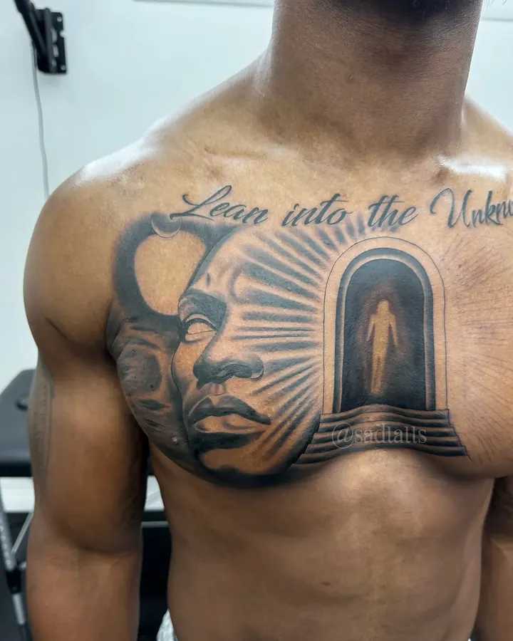 Black and grey tattoo by Dre: face and doorway with script, chest