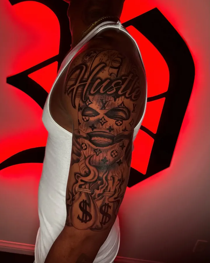 Black and grey tattoo by Dre: hustle lettering, upper arm