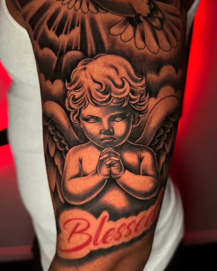Black and grey tattoo by Dre: cherub and clouds, upper arm