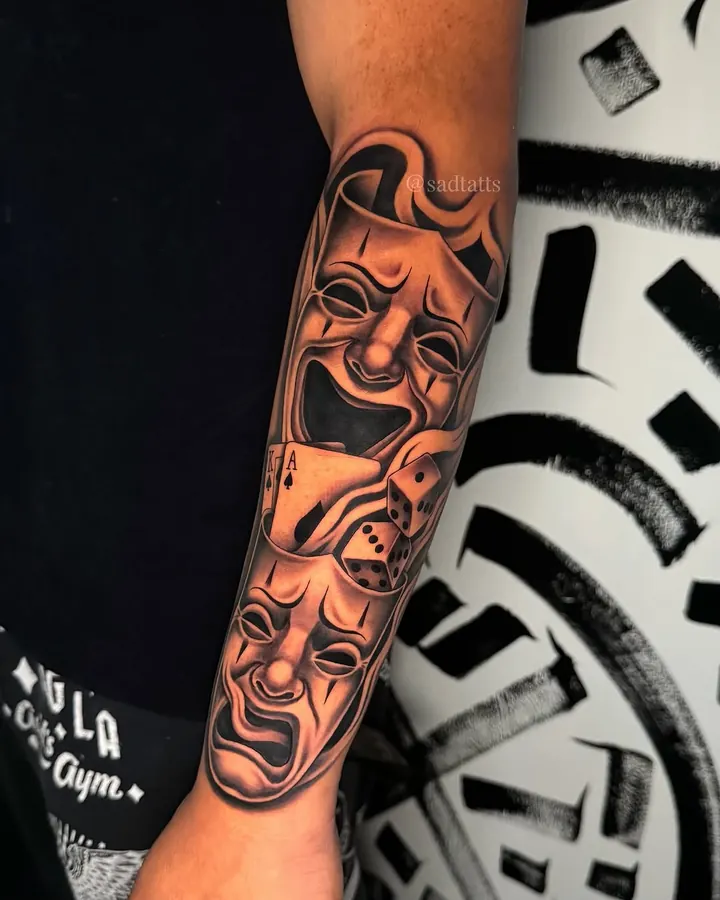 Black and grey tattoo by Dre: comedy and tragedy masks, forearm
