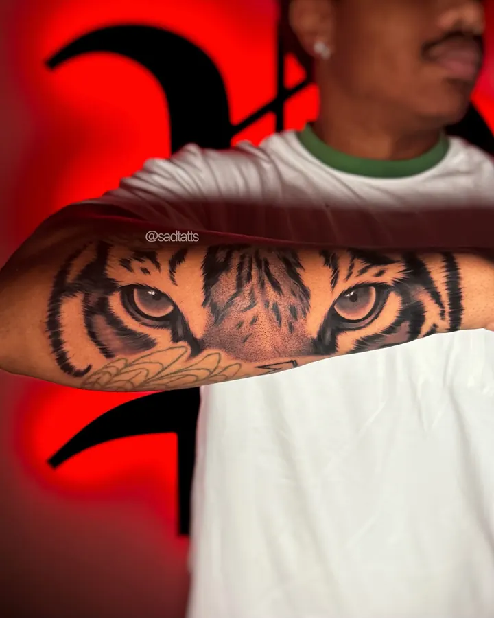 Black and grey tattoo by Dre: tiger eyes, forearm