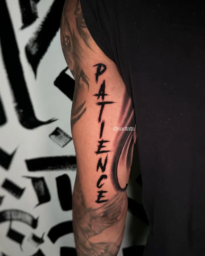 Black and grey tattoo by Dre: patience lettering, arm